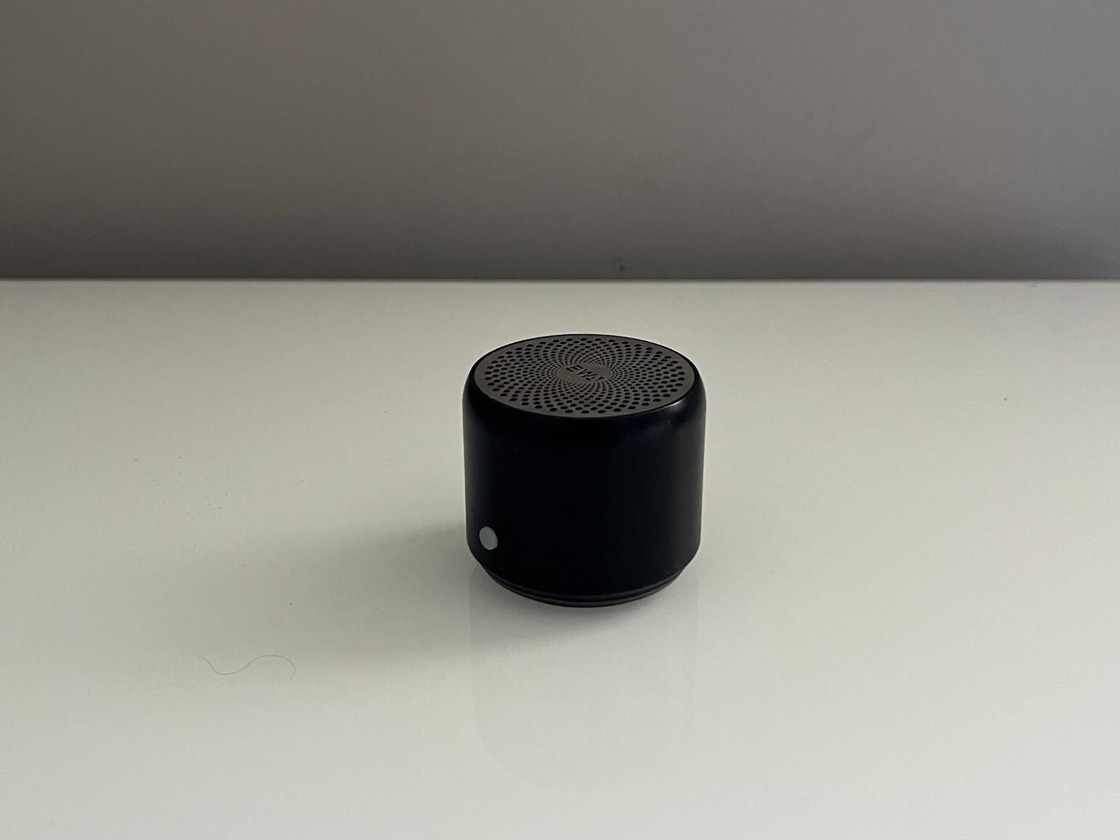 This is another photo of my portable speaker, taken from a lower angle. From this view, you can see the rounded edges of the cylinder better and more of the front part, including the button. The angle also makes a small shadow under the speaker, which gives the image more depth.